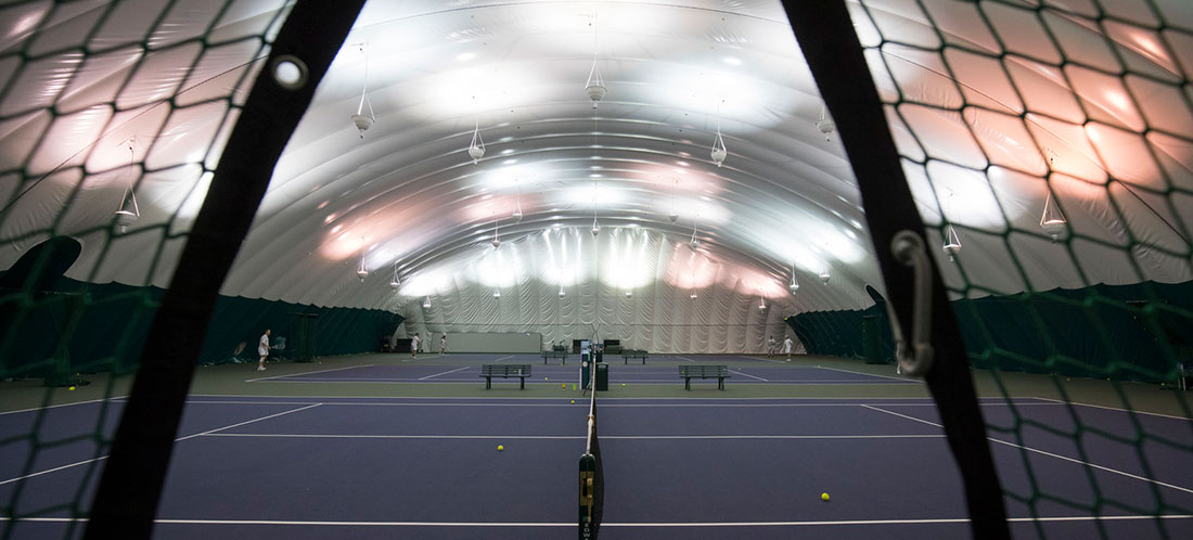 People play tennis on 3 courts inside a green and white indoor dome